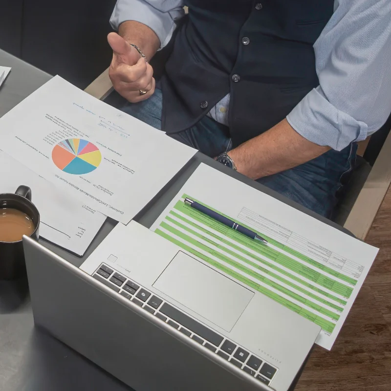 Close-up of a business meeting table with a laptop, coffee mug and financial charts wider