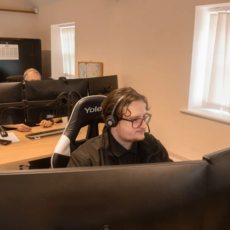 Kristians working at a desk with multiple monitors and a laptop in a well-lit office