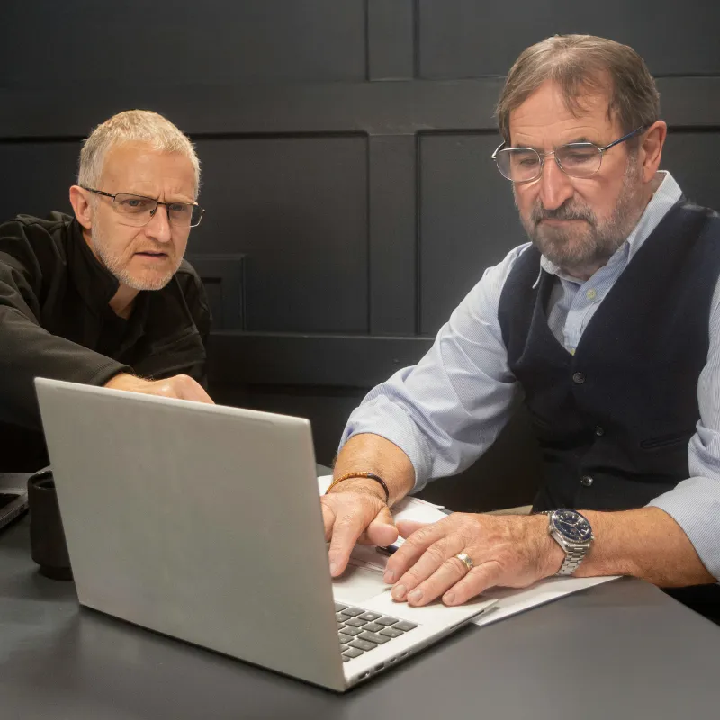 Two men collaborating at a desk, reviewing information on a laptop during a business meeting.