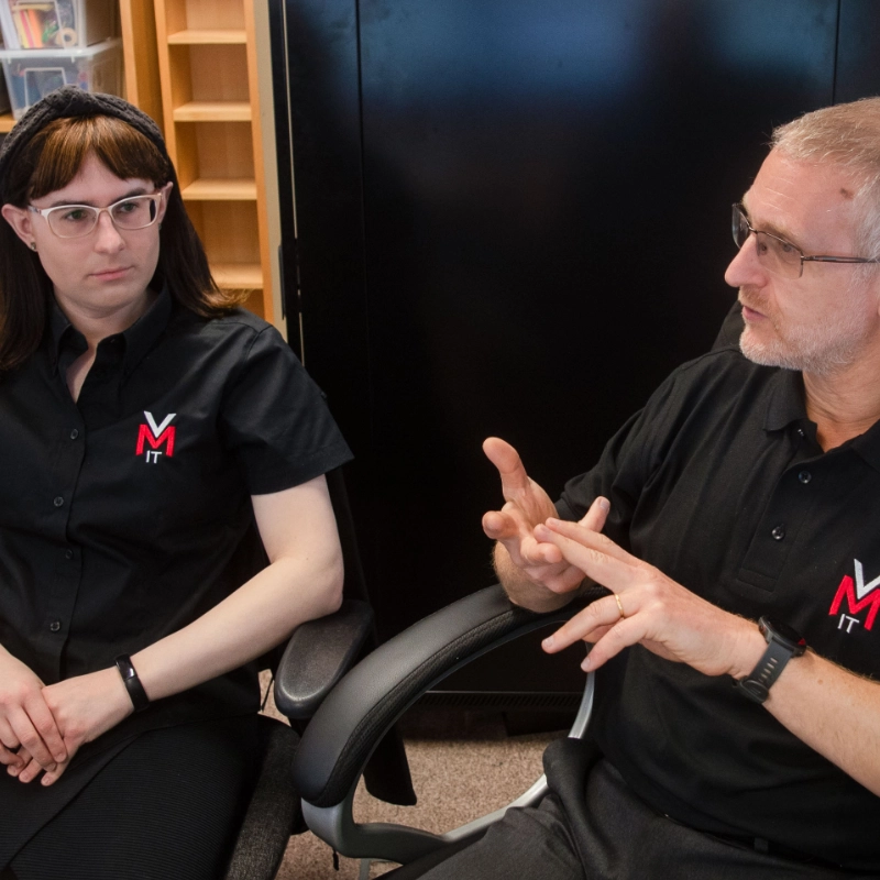 A man and woman sitting in chairs indoors, both wearing casual clothing.